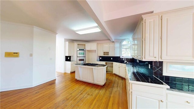 kitchen with decorative backsplash, stainless steel appliances, light hardwood / wood-style floors, tile counters, and a center island