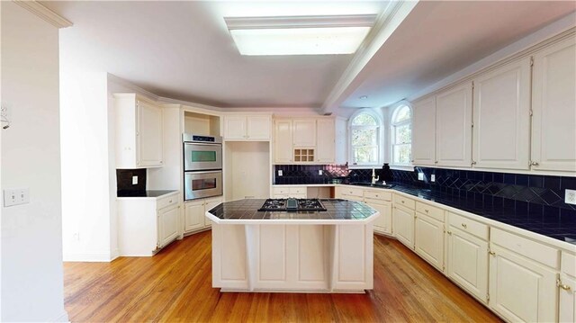 kitchen with backsplash, appliances with stainless steel finishes, light hardwood / wood-style floors, tile counters, and a center island