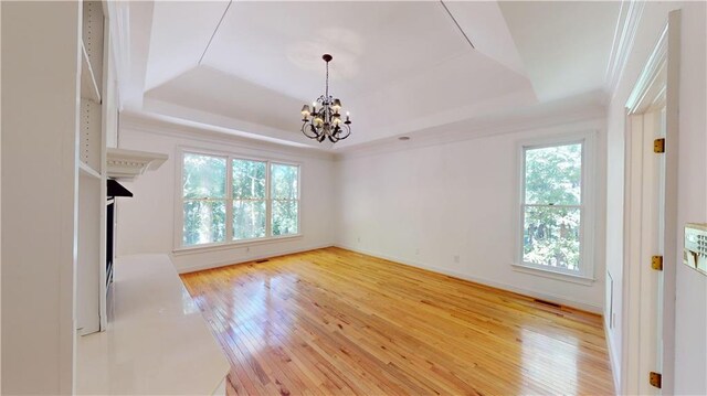 interior space with light hardwood / wood-style flooring, a chandelier, and a raised ceiling