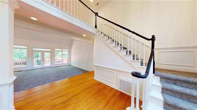 stairs featuring crown molding, french doors, wood-type flooring, and a high ceiling