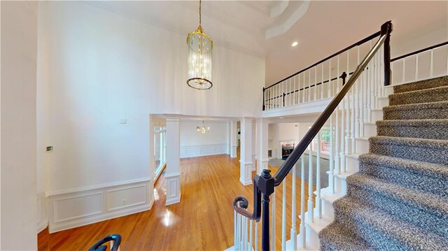 staircase featuring a high ceiling, hardwood / wood-style flooring, a chandelier, and ornate columns