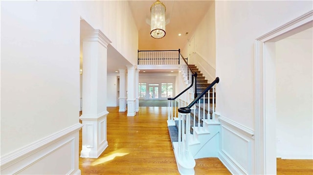 foyer entrance featuring a chandelier, ornate columns, light wood-type flooring, and a high ceiling