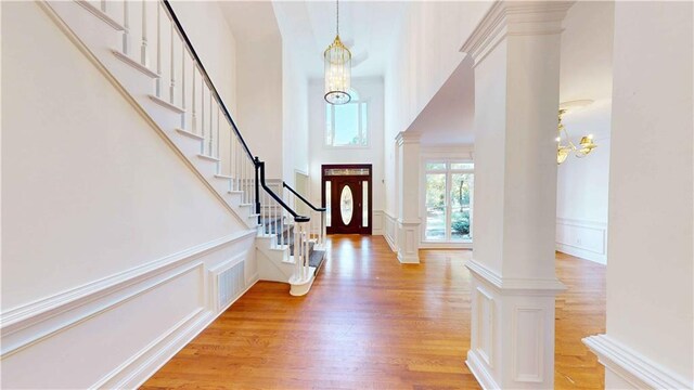 entryway with light hardwood / wood-style flooring, a notable chandelier, ornate columns, and a towering ceiling