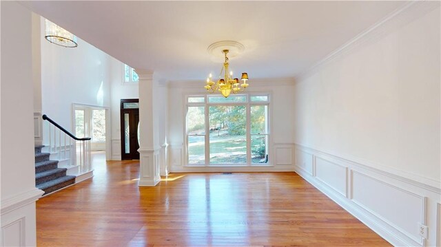 interior space with decorative columns, a notable chandelier, ornamental molding, and light wood-type flooring