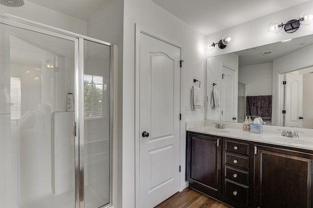 full bath with a stall shower, double vanity, and wood finished floors