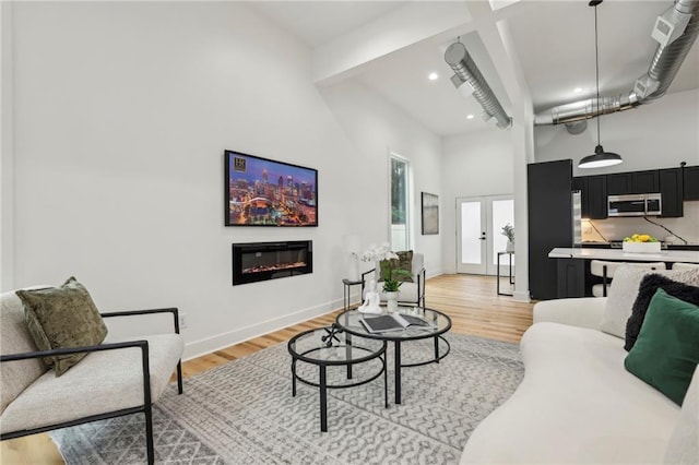 living area featuring light wood-style flooring, a high ceiling, baseboards, french doors, and a glass covered fireplace