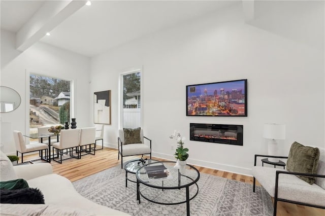 living room featuring beam ceiling, baseboards, wood finished floors, and a glass covered fireplace