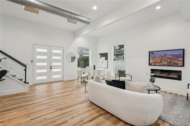 living room featuring a glass covered fireplace, stairway, wood finished floors, french doors, and recessed lighting