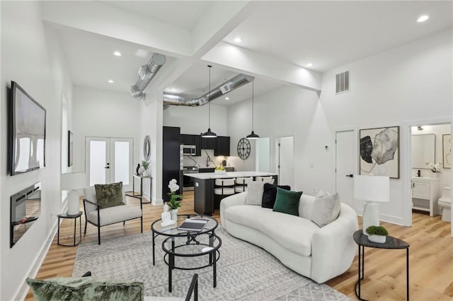 living area with visible vents, a towering ceiling, light wood-style flooring, french doors, and recessed lighting