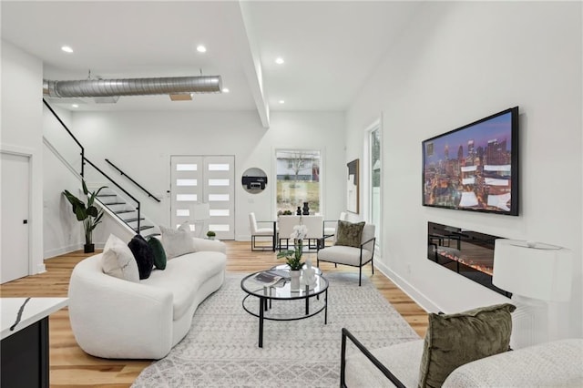 living room with light wood finished floors, stairway, a glass covered fireplace, and recessed lighting