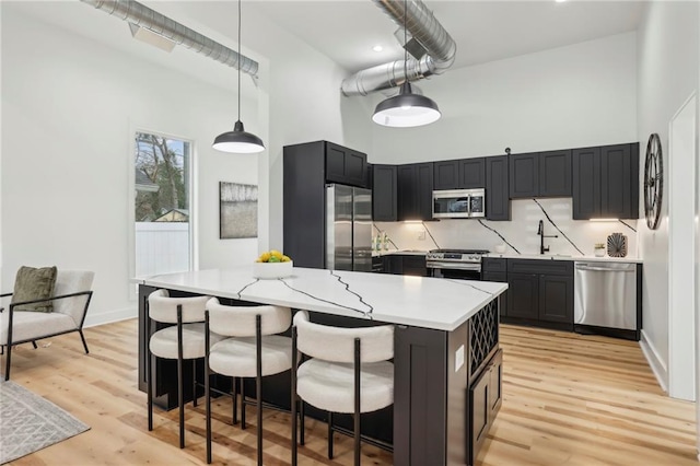 kitchen featuring light wood-style flooring, a high ceiling, stainless steel appliances, and a sink