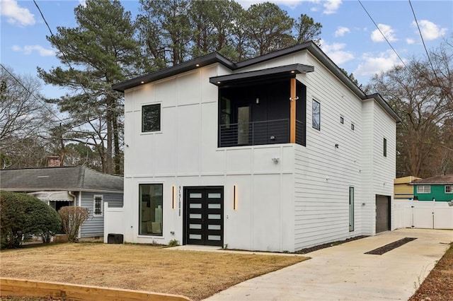 contemporary house featuring an attached garage, a balcony, concrete driveway, board and batten siding, and a front yard