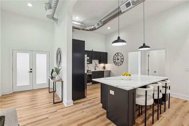 kitchen with light wood finished floors, a breakfast bar area, dark cabinets, a center island, and a high ceiling