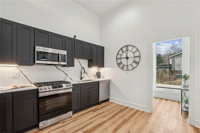 kitchen with baseboards, appliances with stainless steel finishes, light countertops, light wood-style floors, and a sink