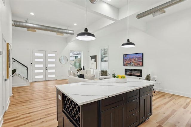 kitchen with hanging light fixtures, a glass covered fireplace, a towering ceiling, and light wood-style floors