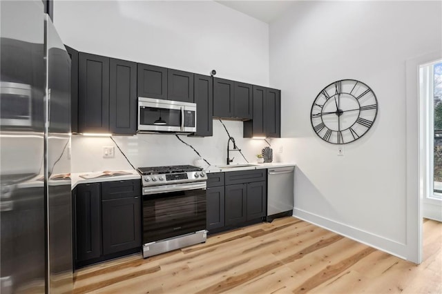 kitchen with baseboards, appliances with stainless steel finishes, light countertops, light wood-style floors, and a sink