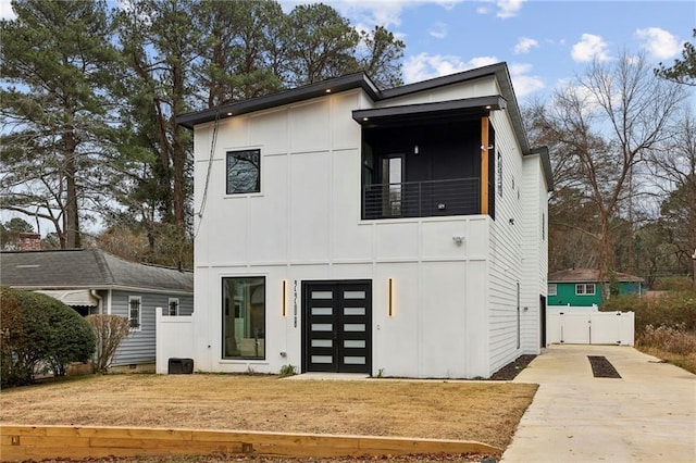 back of house with driveway, a balcony, a gate, a yard, and board and batten siding