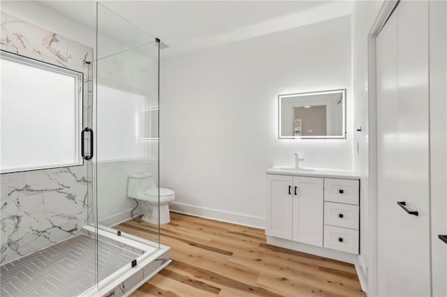 full bath with a marble finish shower, baseboards, toilet, wood finished floors, and vanity