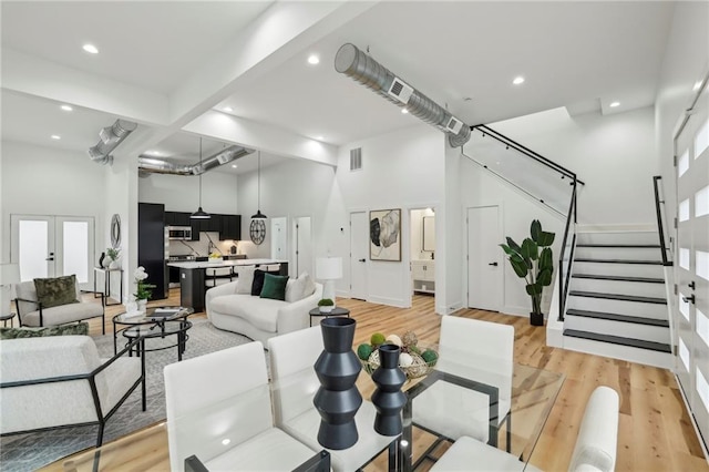 living room featuring light wood-type flooring, a towering ceiling, stairway, and french doors