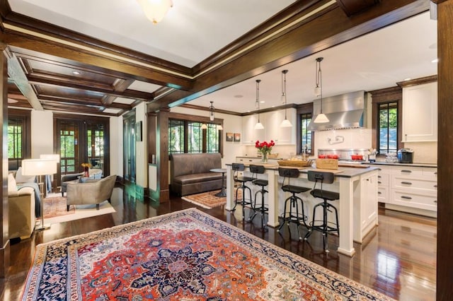 kitchen with white cabinets, a kitchen island, a breakfast bar, hanging light fixtures, and wall chimney range hood