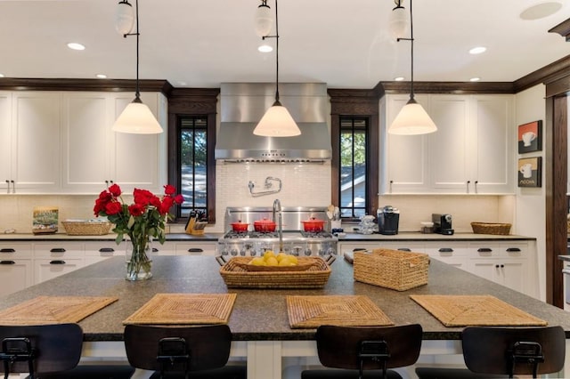 kitchen with a kitchen bar, decorative light fixtures, wall chimney exhaust hood, and stove