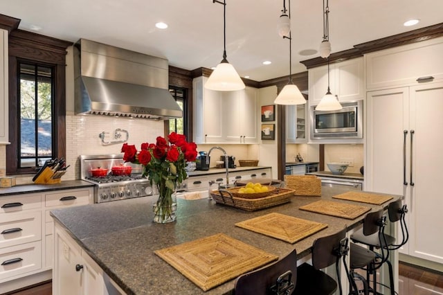 kitchen featuring pendant lighting, stainless steel microwave, stove, white cabinets, and wall chimney exhaust hood