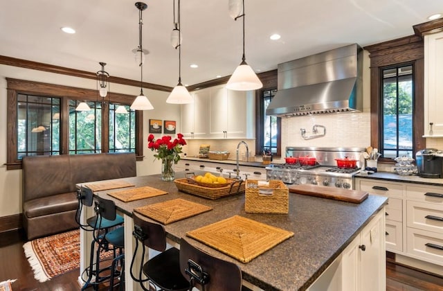 kitchen with white cabinetry, backsplash, dark wood-style floors, wall chimney exhaust hood, and pendant lighting