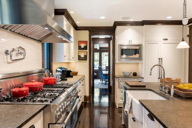 kitchen featuring white cabinets, appliances with stainless steel finishes, hanging light fixtures, range hood, and a sink