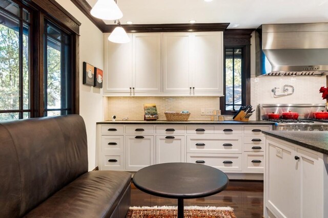 kitchen with wall chimney range hood, white cabinets, decorative backsplash, and decorative light fixtures