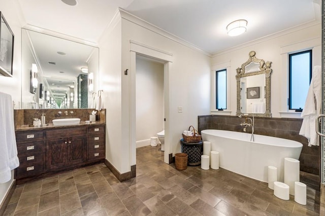 full bathroom with toilet, crown molding, vanity, a freestanding tub, and tile walls