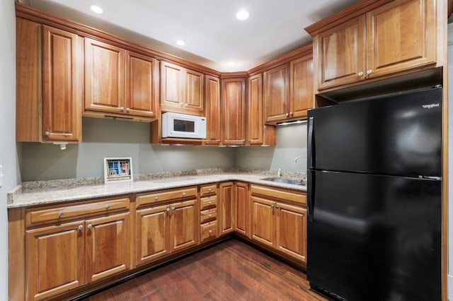 kitchen with dark wood finished floors, white microwave, freestanding refrigerator, light stone countertops, and a sink