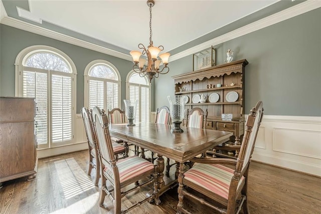 dining room featuring wood finished floors, ornamental molding, wainscoting, a decorative wall, and a notable chandelier