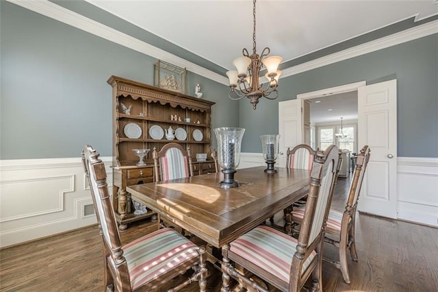 dining space with dark wood finished floors, a notable chandelier, ornamental molding, and a wainscoted wall