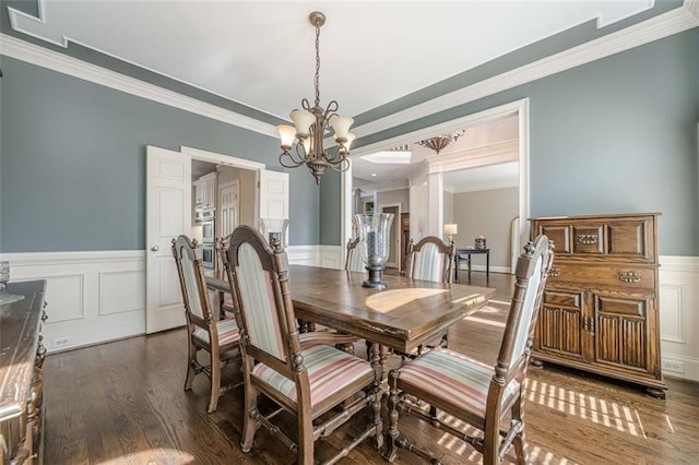 dining area with a wainscoted wall, a chandelier, dark wood-style flooring, and ornamental molding