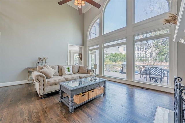 living room with ornamental molding, ceiling fan, dark wood finished floors, baseboards, and a towering ceiling