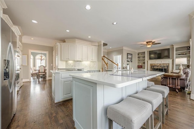 kitchen with dark wood-style floors, stainless steel refrigerator with ice dispenser, a ceiling fan, and a kitchen island with sink