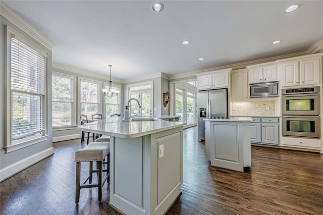 kitchen featuring a kitchen island with sink, ornamental molding, a sink, stainless steel appliances, and an inviting chandelier