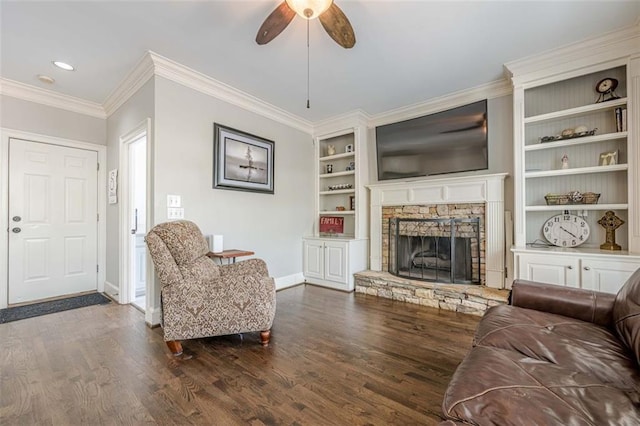 living room with baseboards, ceiling fan, ornamental molding, a stone fireplace, and wood finished floors