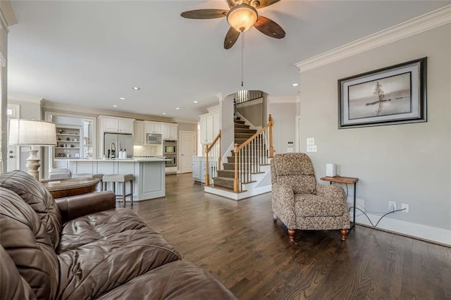 living room featuring stairs, dark wood-type flooring, crown molding, and a ceiling fan