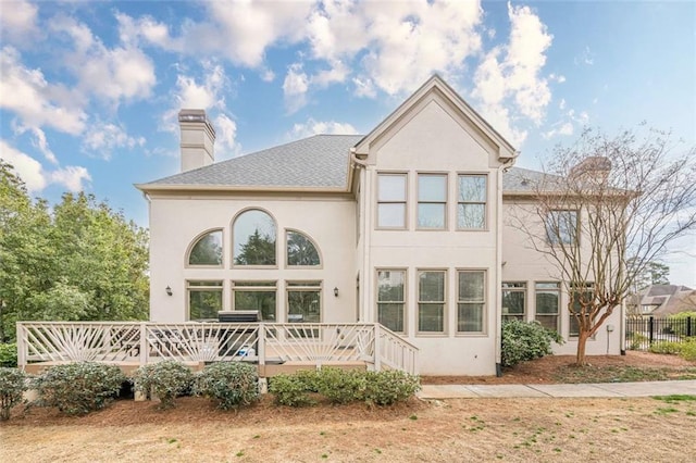 rear view of property featuring a shingled roof, fence, stucco siding, a chimney, and a deck