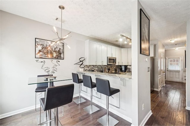 kitchen featuring a breakfast bar, light stone counters, a textured ceiling, kitchen peninsula, and white cabinets