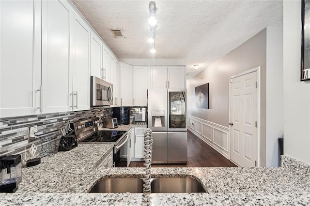 kitchen with appliances with stainless steel finishes, rail lighting, white cabinets, light stone counters, and a textured ceiling