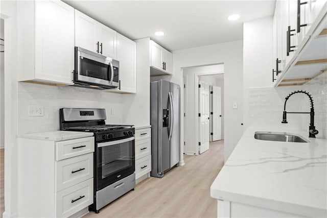 kitchen featuring stainless steel appliances, white cabinetry, a sink, and light stone counters