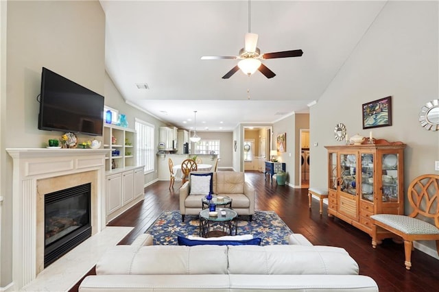 living room with dark wood-type flooring, ceiling fan, high vaulted ceiling, a high end fireplace, and washer / clothes dryer