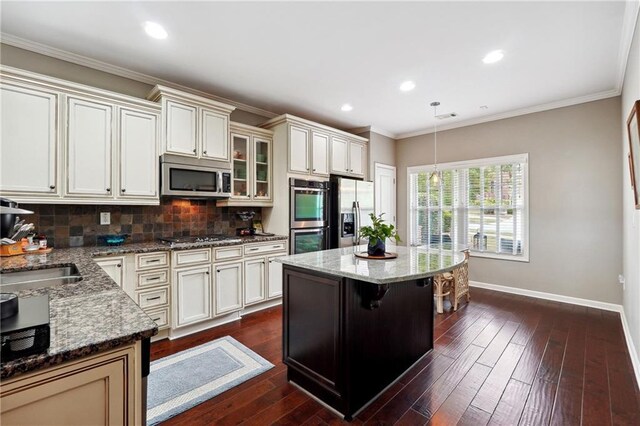 kitchen featuring a center island, appliances with stainless steel finishes, a kitchen breakfast bar, pendant lighting, and light stone countertops