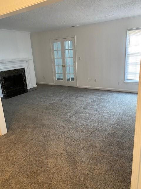 unfurnished living room with french doors, a textured ceiling, and dark colored carpet