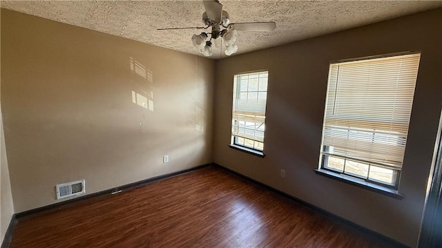 unfurnished room featuring visible vents, a ceiling fan, a textured ceiling, dark wood-style floors, and baseboards