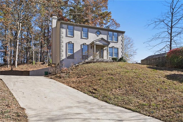 colonial home with concrete driveway, fence, a chimney, and stucco siding