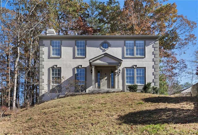 colonial-style house featuring a front yard and stucco siding