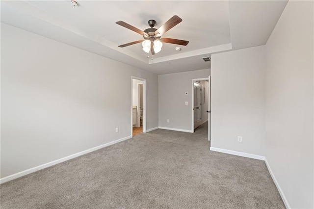 carpeted spare room with visible vents, baseboards, a raised ceiling, and a ceiling fan